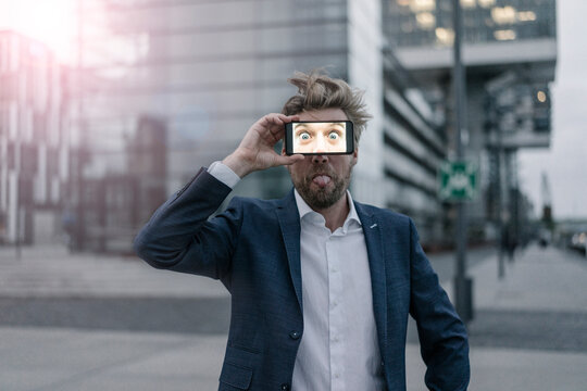 Playful businessman holding cell phone in front of his eyes