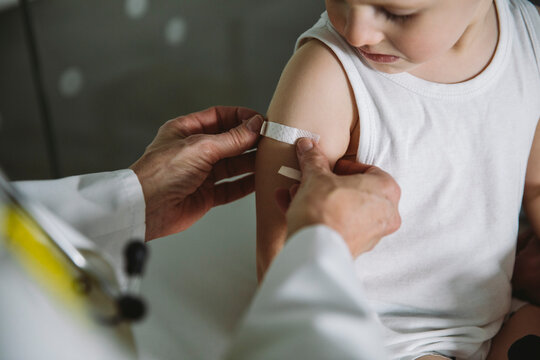 Pediatrist putting band-aid onto arm of toddler after vaccination
