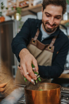 Smiling chef putting chopped vegetables in cooper saucepan while making Broth soup standing in kitchen