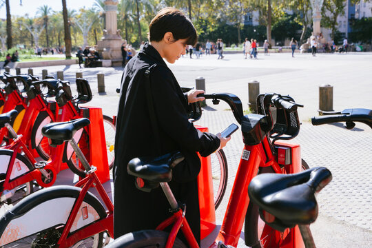 Woman renting bicycle through smart phone at parking station