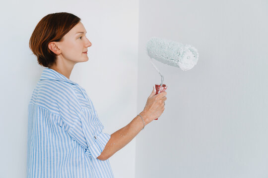 Woman paints a white wall with a roller during home renovation