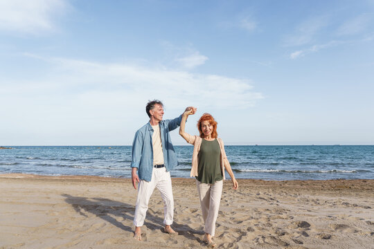 Senior couple dances barefoot on the beach during summer vacation