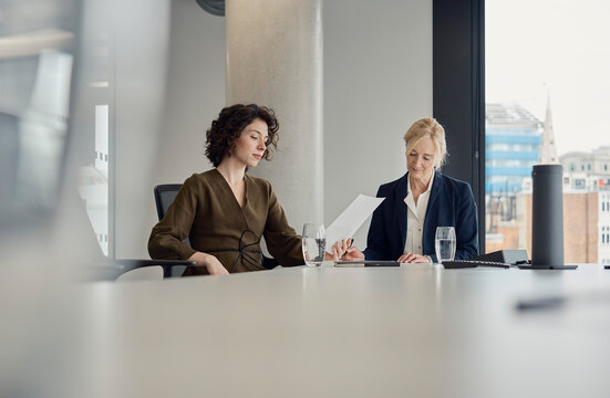 Businesswoman and colleague read document in London office boardroom