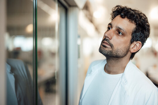 Scientist in lab coat looking through glass window in hospital