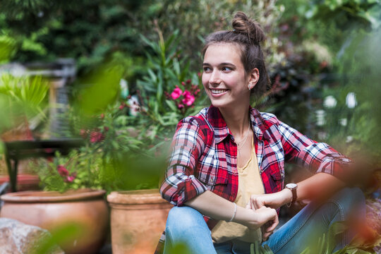 Smiling woman sits in a lush summer garden at home