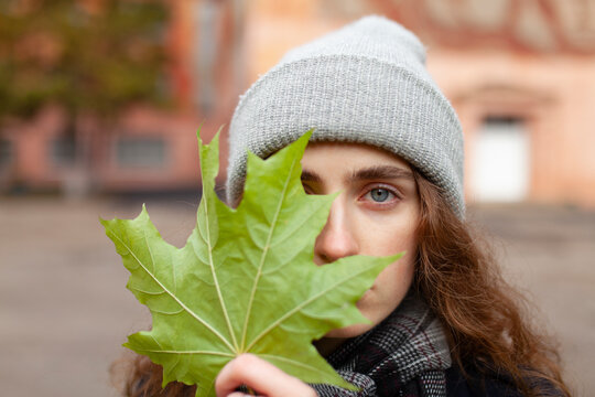 Woman outdoors hiding her face behind a green maple leaf in autumn
