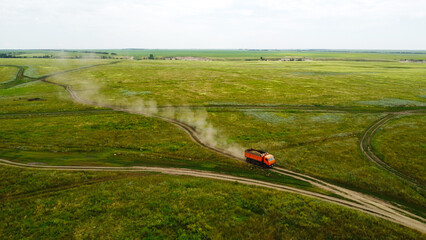 Aerial view of a heavy dump truck driving on a dirt road through a rural village settlement © Andrey