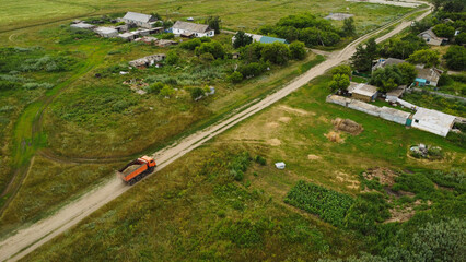 Aerial view of a heavy dump truck driving on a dirt road through a rural village settlement © Andrey