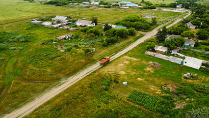 Aerial view of a heavy dump truck driving on a dirt road through a rural village settlement © Andrey