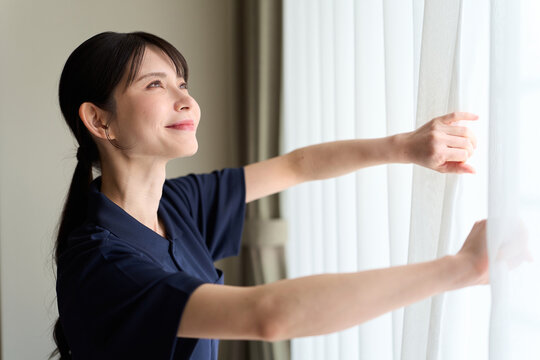 客室のカーテンを開ける清掃業の女性