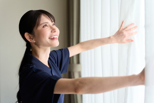 客室のカーテンを開ける清掃業の女性