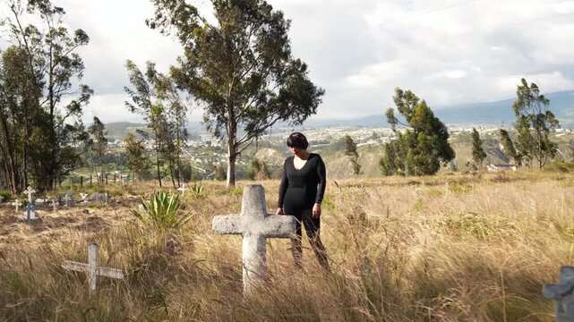 Grieving woman dressed in black visiting grave at a windy cemetery expressing remembrance