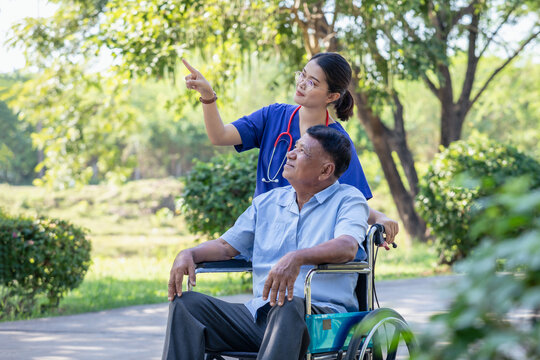 Smiling female nurse caregiver and senior man in wheelchair with sunny park. Positive image depicting dedicated professional care.