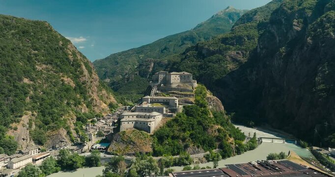 Historic Fort Bard rises above the Aosta Valley on a rocky hill, surrounded by majestic mountains and a winding river. A breathtaking Italian landmark in a spectacular alpine setting.