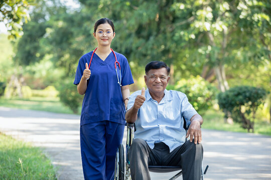 Female nurse cares for elderly man sitting in wheelchair in park. Positive image depicting dedicated professional care for an elderly patient in a natural outdoor setting.
