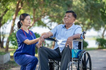 Obraz premium Female nurse cares for elderly man sitting in wheelchair in park at nursing home, feeling sad.