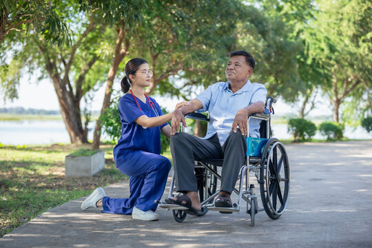 Elderly man patient in a wheelchair being cared for by a medical professional. Asian nurse take care senior male sit on wheelchair in park, outdoor.