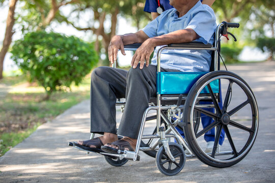 Elderly male patient in a wheelchair being cared for by a medical professional in a park setting, close up