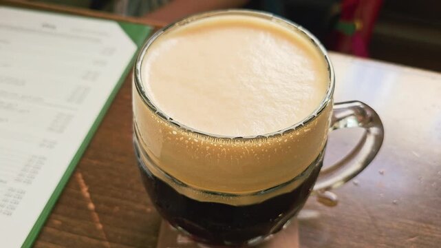 Person grabs a frothy dark beer mug at a restaurant table, with golden foam, chilled glass, condensation drops, warm indoor lighting, and casual social drinking atmosphere at night.