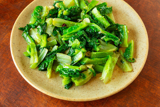 Authentic Chinese stir-fried romaine lettuce with salt only. A healthy, fresh, and savory Asian vegetable dish.  Rustic brown wooden background. 