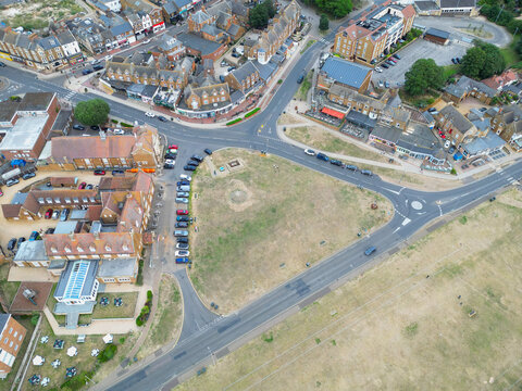 Town centre view of the popular seaside town. Showing the parched green space and large hotel and cars on the left. To the top are rows of shops.