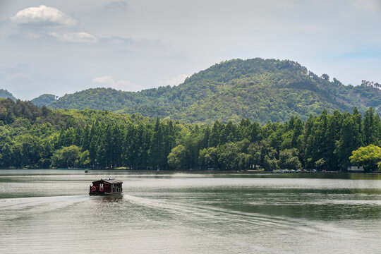 Traditional Dark Wood Tour Boat Navigating West Lake Against Forested Mountains at Daytime in Hangzhou, Zhejiang, China