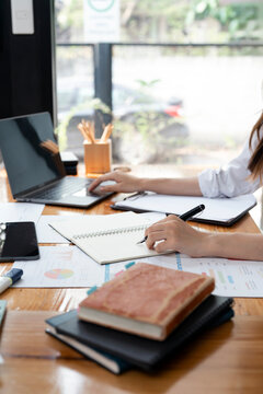 Businesswoman working on laptop and writing on notebook at wooden desk