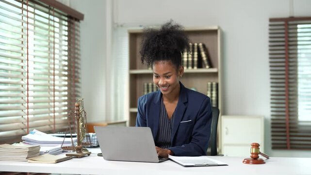 Professional African American female lawyer working in her office, using a laptop for legal research and documentation, then talking on the phone with a client for legal consultation