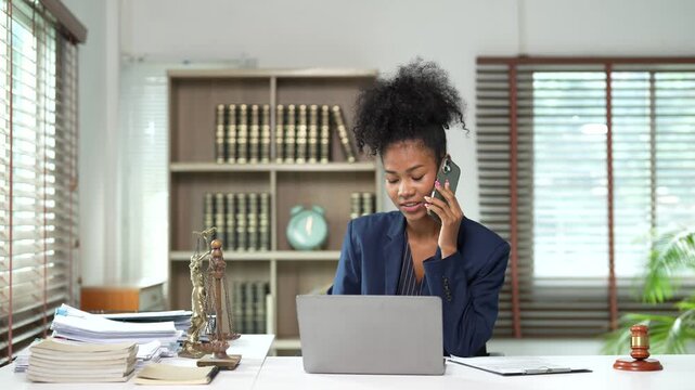 African American businesswoman lawyer talking on the phone and working on her laptop in an office, legal professional providing consultation and smiling with confidence