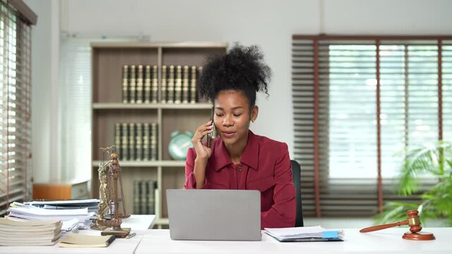 Professional african american female lawyer talking on the phone with a client while working on her laptop and providing legal advice and business consulting in her office