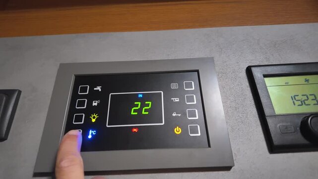 Close-up of a person's finger using the touch screen control panel in a modern rv, switching between internal and external temperature displays on the digital thermostat for climate control