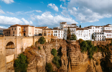 Fototapeta premium Ronda's old town architecture and iconic bridge span cliffs over the El Tajo gorge in Andalucia, Spain, showcasing a dramatic landscape and historic urban planning against a blue sky