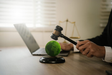 Judge's gavel striking a green Earth symbol, representing environmental law, climate justice, sustainability regulations, and global governance. © Natthawadee