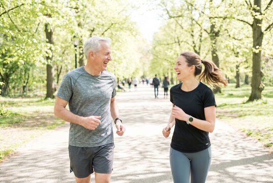 Father and adult daughter jogging together in bright park, active lifestyle across generations