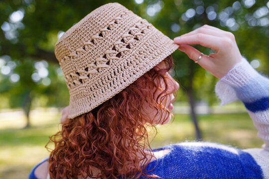 Redhead girl in beige whickered hat and blue sweater posing back and side view to camera, close up shot. Clothing and accessories
