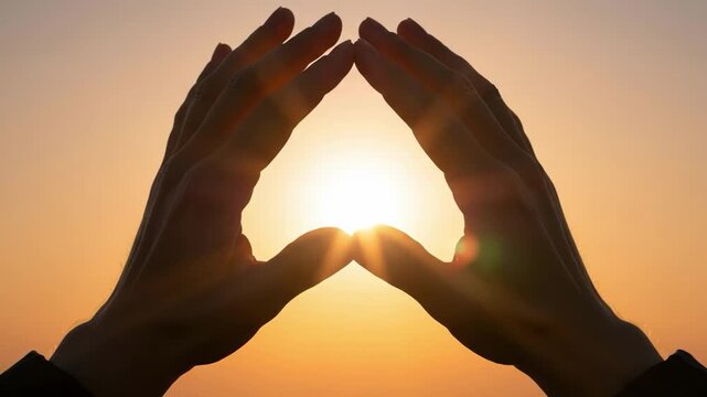 Silhouette of hands framing the sun at sunset