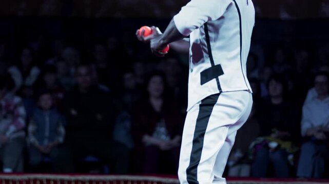 Professional performer juggling orange balls on stage, engaging entertainment act during live show, dark skin man performing, audience background, dynamic movement slow motion