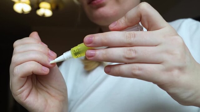 Woman applying nourishing oil on cuticles using a convenient nail cuticle oil pen with brush. Professional home manicure, hand skin health care and treatment.