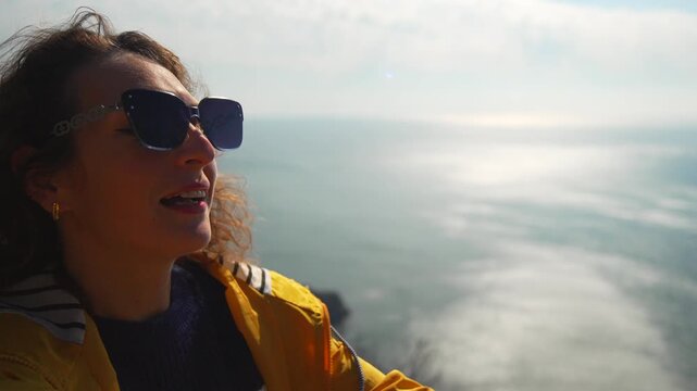 Woman viewpoint sea. Young woman in a yellow raincoat standing on a high cliff overlooking a foggy ocean while gesturing with joy
