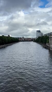 Calm river flowing through urban landscape under cloudy sky  