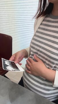 エコー写真を見ながらお腹を撫でる妊婦