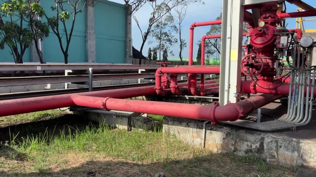 Red hydrant pipes stretch across concrete and grass