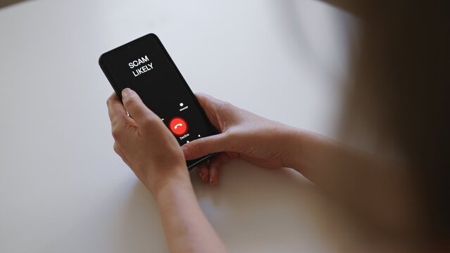 Woman holding smartphone with incoming scam call on screen.