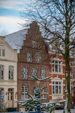 Winter scene in Friedrichstadt, Germany, with historic step-gabled brick houses covered in snow and small decorated Christmas tree in the foreground.
