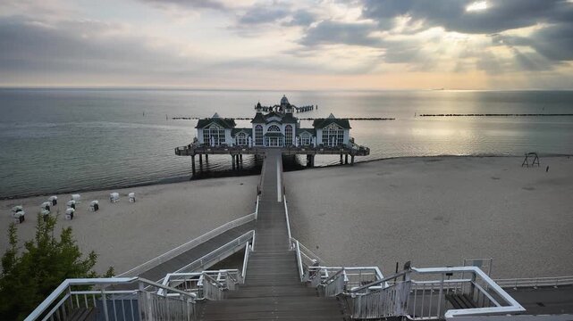 Timelapse of sunrise by historic pier in Sellin on the island of Rugen, Germany, stretching into the Baltic Sea with beach chairs on the sand.