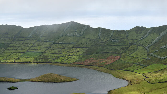 Volcanic crater lake with terraced fields and small islands on a misty day