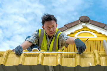 Asian male roofer or construction worker in safety helmet using tape measure to take measurements on a residential roof for repair and renovation project © Jack Tamrong
