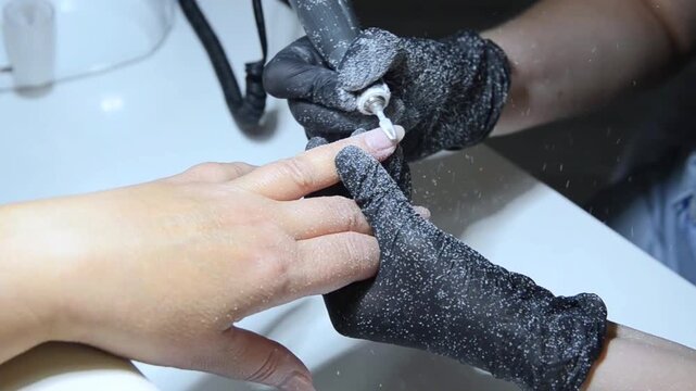 Close-up of a professional nail technician removing old gel polish with an electric nail drill and ceramic drill bit during a manicure procedure.