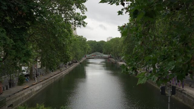 Canal Saint Martin water channel features a pedestrian bridge and trees in Paris France. European urban historical landscape for travel navigation transport and residential district tourism.