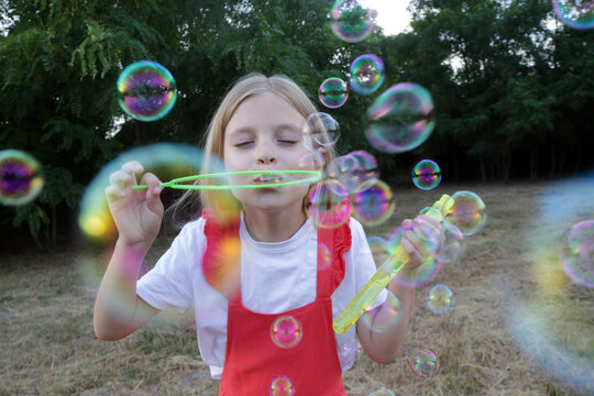 Happy little girl blowing soap bubbles on a sunny summer day